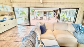 Un salón amplio con un sofá beige, un aparador blanco con adornos, y vistas a un patio exterior.