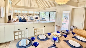 Una cocina amplia con una isla grande, un comedor con cristalería azul y un espacio habitable luminoso y abierto con vistas al exterior.