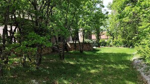 A lush garden with stone walls and trees, a stone bench, and a grassy area.