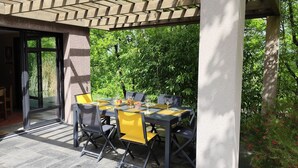 An outdoor patio with a table and chairs, a pergola, and a view of greenery.