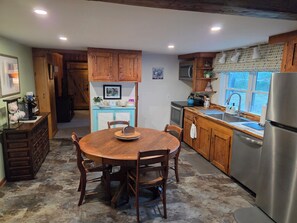 A kitchen with wooden cabinets, a dining table, chairs, a refrigerator, and a window with a view.