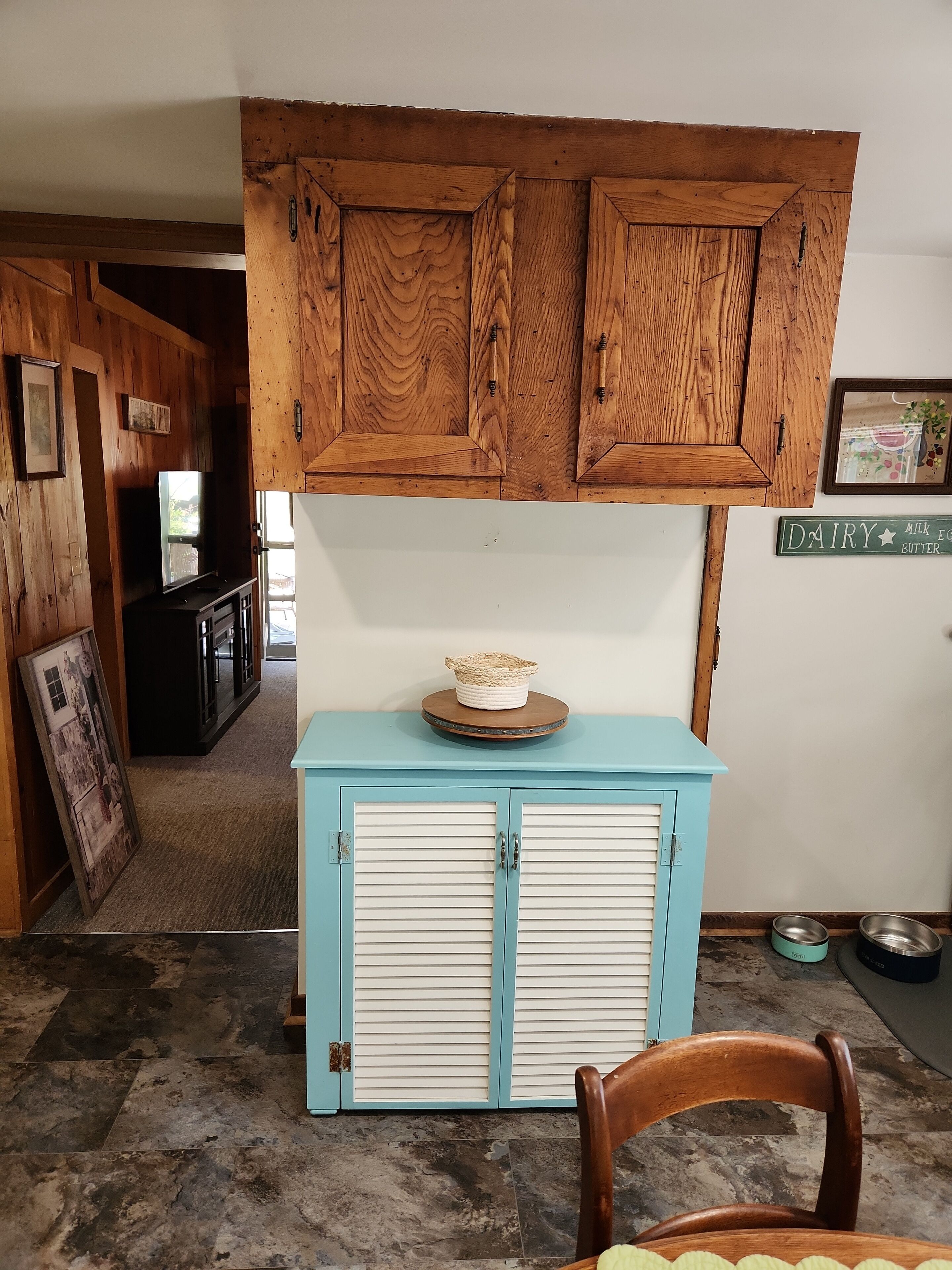 Une pièce comprenant un meuble en bois, une commode bleue, un tableau encadré et une chaise en bois.