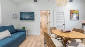 Un salon moderne avec un canapé bleu, une table à manger entourée de chaises en osier, un lustre et des œuvres d’art accrochées aux murs.