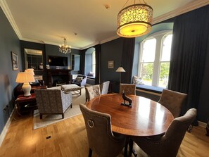 A dining area with a round table, upholstered chairs, a chandelier, and a fireplace.