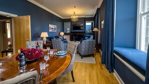 Un coin repas avec une table ronde en bois, des chaises et un lustre. On y trouve également une cheminée et un téléviseur fixé au mur.