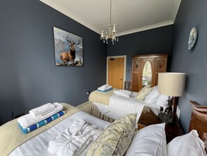 A hotel room with two beds, a chandelier, a painting of a deer, and a mirror on the wall.