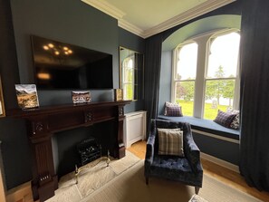 A room with a fireplace, a television, a window seat with cushions, and a view of the outdoors. - Monastery 8 - Paterson 2 bedroom apartment with luxury period features (Fort Augustus)