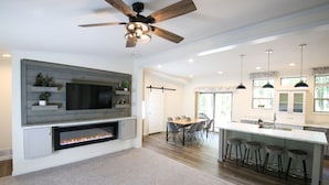A modern kitchen with a built-in fireplace, a dining area with a wooden table and chairs, and a bar area with stools.