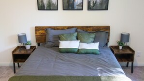 A bedroom with a large bed, two nightstands, a wooden headboard, and three framed pictures on the wall.