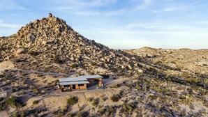 A modern building with a flat roof, surrounded by a rocky desert landscape. - Rocky Roost: Cowboy Tub, Hot Tub, AC & Stargazing (Yucca Valley)