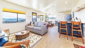 A modern living room with a sofa, coffee table, and dining area with chairs. - Rocky Roost: Cowboy Tub, Hot Tub, AC & Stargazing (Yucca Valley)