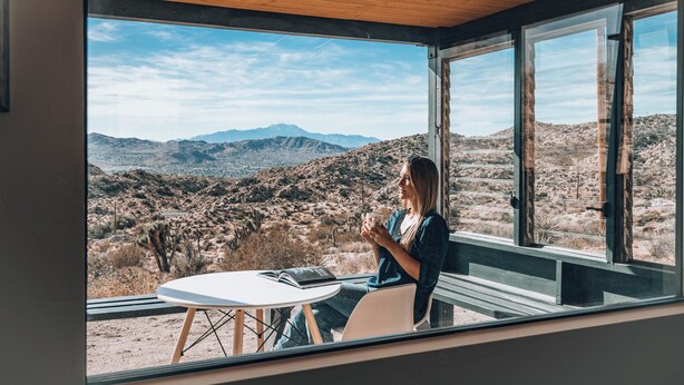 A room with a large window offering a view of a desert landscape with mountains. - Rocky Roost: Cowboy Tub, Hot Tub, AC & Stargazing (Yucca Valley)