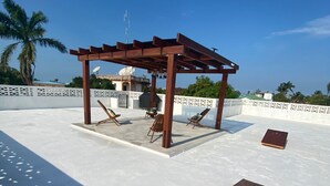 Una terraza en la azotea con una pérgola de madera, dos sillones y una mesita.