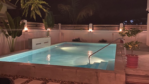 Una piscina rectangular con superficie de agua azul cristalina, rodeada por un borde de piedrecitas y un sendero de piedra que lleva a ella.