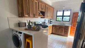 Una cocina con armarios de madera, lavadora, ventilador de techo y ventana que proporciona luz natural.