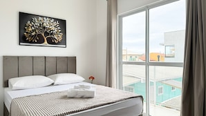Een hotelkamer met een bed, een lijst met kunstwerk erboven en een groot raam met gordijnen.