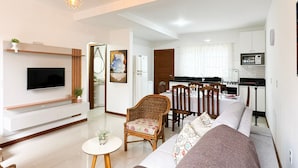 Een moderne woonkamer met een flatscreen televisie, een bank, een eettafel met stoelen en een keuken met een fornuis en magnetron.