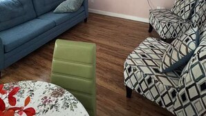 Ett vardagsrum med en takfläkt, en platt-TV som är monterad på väggen, en blå soffa, en mönstrad fåtölj och en grön pall.