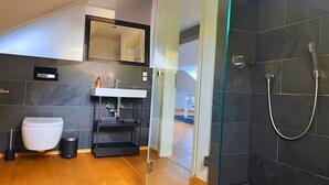 A modern bathroom with a glass shower enclosure, a white toilet, and a black sink vanity. - Modern loft in the center of Hattingen (Hattingen)
