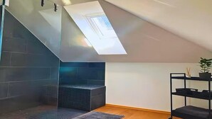 A modern attic room with a skylight, a glass shower enclosure, and a black metal shelf with a plant. - Modern loft in the center of Hattingen (Hattingen)