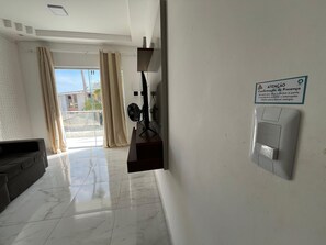 A hotel lobby with a sofa, a fan, a sign, and a door with a security panel. - Condomínio com Piscina á 500m da Praia (Porto Seguro)