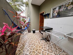 A tiled patio with a metal drying rack, a hammock, and potted plants. - Condomínio com Piscina á 500m da Praia (Porto Seguro)