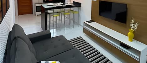 Un salon moderne avec un canapé gris, un téléviseur à écran plat posé sur un meuble télé en bois, et un vase jaune sur le meuble.