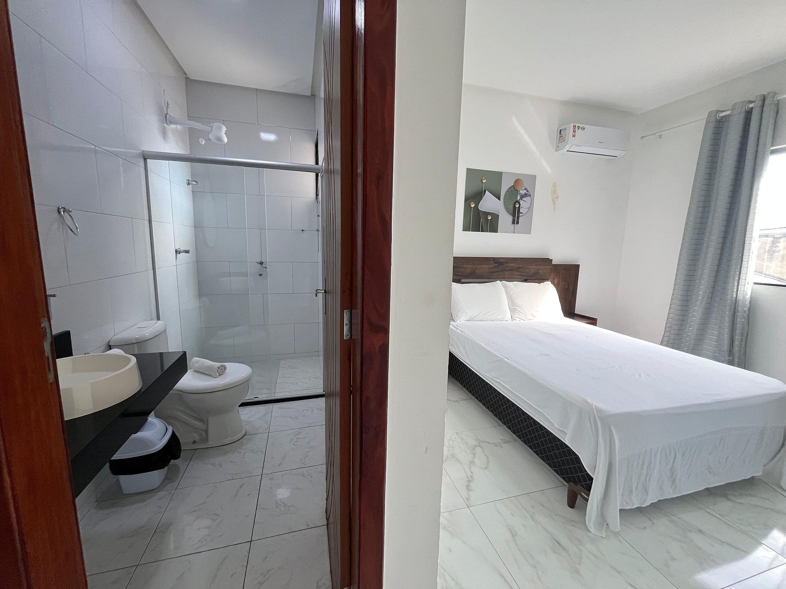 Quarto de hotel com chuveiro, vaso sanitário e uma cama.