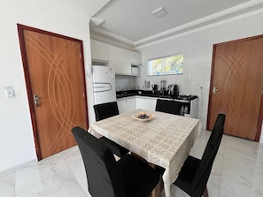 Cocina compacta con muebles blancos, refrigerador, estufa y ventana sobre el fregadero.