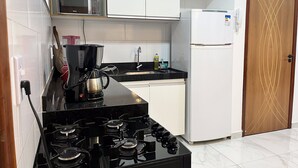A compact kitchen with a gas stove, a microwave, a refrigerator, and a coffee maker. - Condomínio com Piscina á 500m da Praia (Porto Seguro)