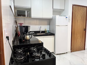Una cocina compacta equipada con estufa a gas, microondas, refrigerador y cafetera.