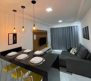 Una sala de estar moderna con un sofá, una mesa de comedor con platos y lámparas colgantes.
