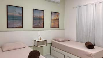 Un dormitorio con dos camas, una mesita de noche, un aire acondicionado de pared y una ventana con cortinas.