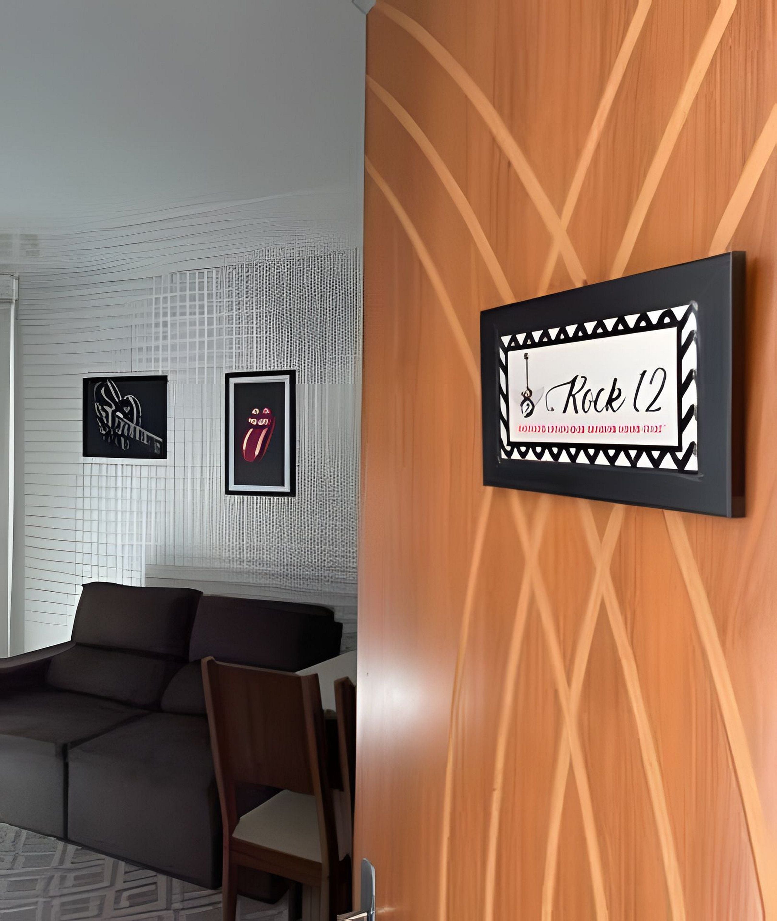 Um quarto com um sofá cinzento, uma parede de madeira com um letreiro emoldurado 'Rock 12' e dois posters emoldurados na parede.
