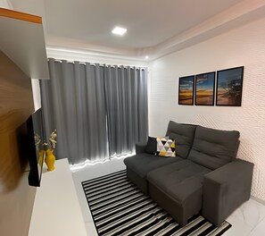 A modern living room with a grey sofa, a striped rug, and a flat-screen TV.