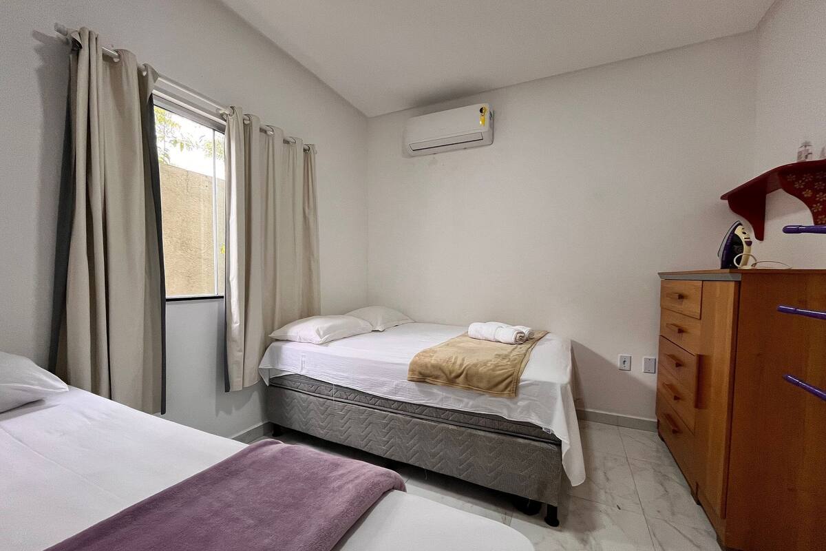 A hotel room with two beds, a wooden dresser, and an air conditioning unit on the wall.