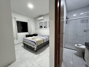 Um banheiro moderno com chuveiro, vaso sanitário e cama com colcha listrada.