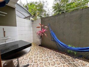 A tiled patio with a hammock, a grill, and a potted plant.