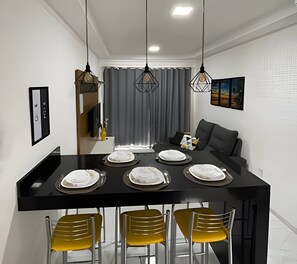 A modern dining area with a black table set for six, yellow chairs, and pendant lights. - Condomínio com Piscina á 500m da Praia (Porto Seguro)