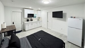 A compact, modern apartment with a kitchenette, a bed, a TV, and a refrigerator. - Charming Studio Apartment at Lake Worth Beach! (Lake Worth Beach)