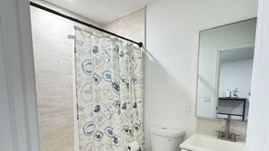 A bathroom with a shower curtain, toilet, sink, and mirror. - Charming Studio Apartment at Lake Worth Beach! (Lake Worth Beach)