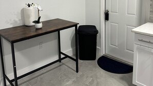A small, clean room with a wooden table, a trash bin, and a white door. - Charming Studio Apartment at Lake Worth Beach! (Lake Worth Beach)