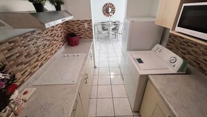 Una cocina compacta con estufa integrada, microondas y un pequeño comedor con mesa y sillas.
