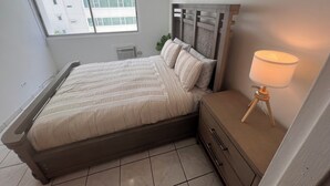 Un dormitorio con cama, mesita de noche, lámpara y ventana con vistas a edificios.