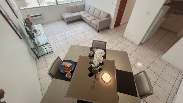 Un área de comedor con una mesa, sillas y una taza de café. Se ve un sofá al fondo, y una ventana ofrece vistas al exterior.