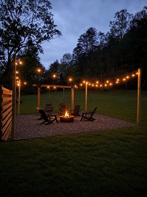 An outdoor seating area with a fire pit, wooden chairs, and string lights.