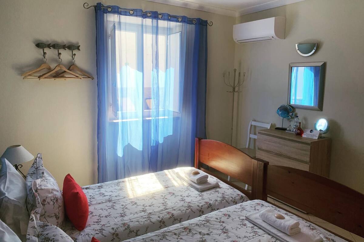 Habitación de hotel con dos camas, un aparador de madera, un equipo de aire acondicionado, un espejo y una ventana con cortina azul.