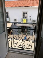 Un balcón con barandilla de hierro forjado, un edificio con techo de tejas rojas y un letrero que dice 'MARCELA'.