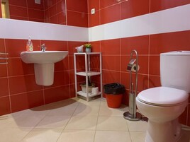 A bathroom with red tiles, a white sink, a toilet, and a shelf with toiletries.