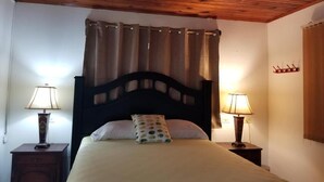 A bedroom with a wooden ceiling, a bed with a headboard, two bedside tables with lamps, and a curtain. - La Estancia del Bosque  (Siguatepeque)